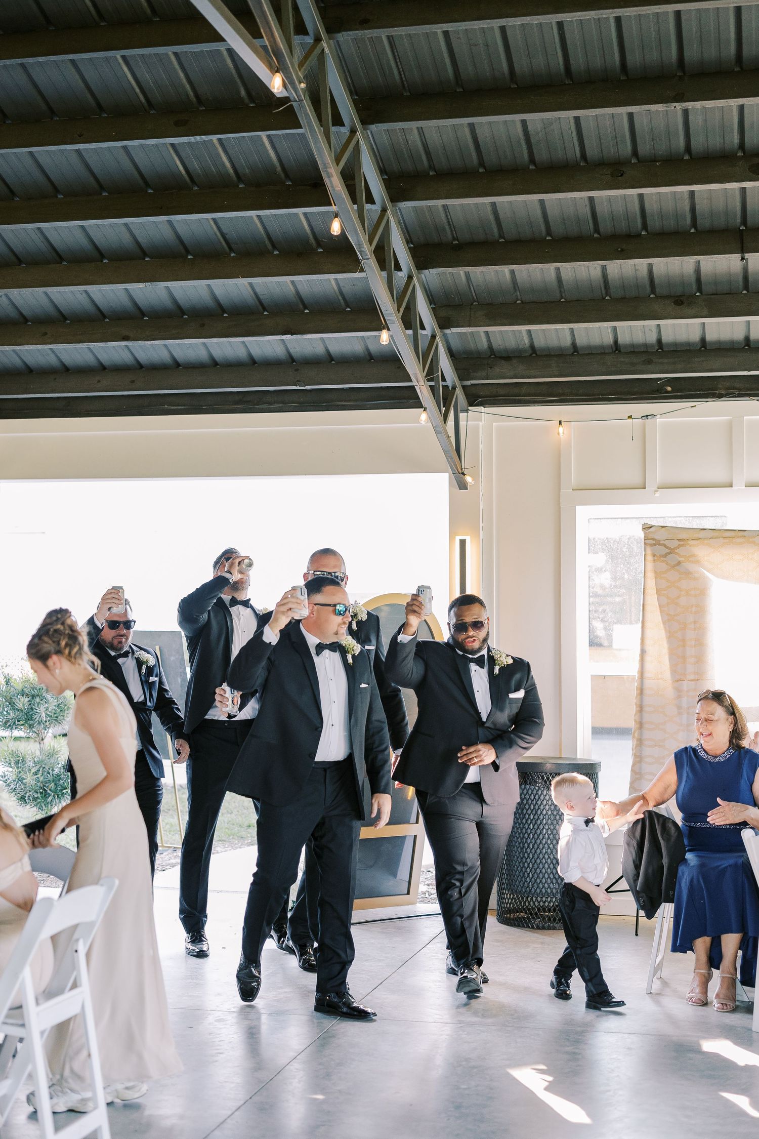 Sequence of wedding party guests in formal attire performing a synchronized line dance in an indoor venue.