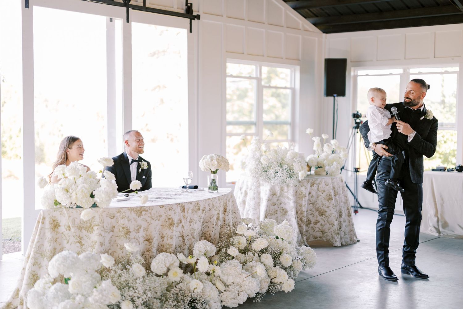 Wedding photographer at work capturing a reception table decorated with white hydrangeas in an elegant white venue.