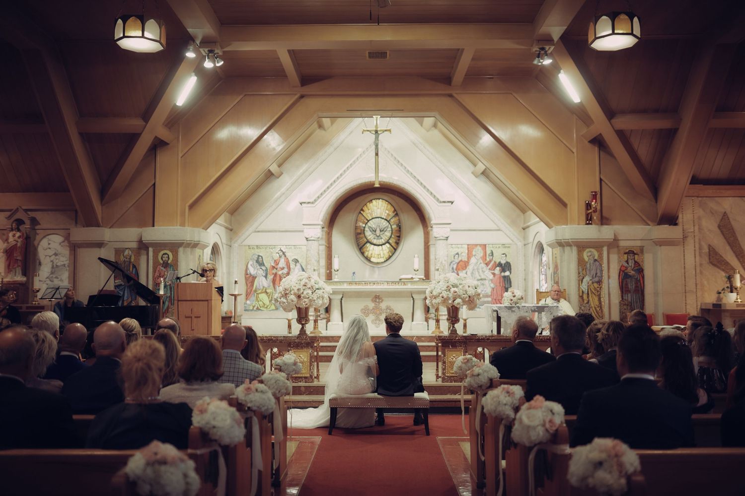 Church wedding ceremony with guests seated in wooden pews as evening light streams through stained glass windows in Banff and Fairmont