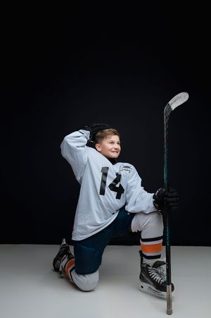 Young hockey player in white jersey and blue pants practicing stick handling skills in a dramatic studio setting.