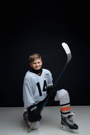 A young skater in a white jersey poses with hockey gear and ice skates against a black background in studio portraits.