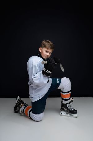 A hockey player in white attire demonstrates proper skate lacing technique on dark background.