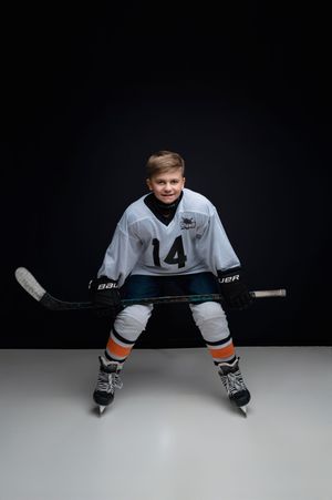 A hockey player in white jersey number 4 poses in a split position on ice against a dark background.