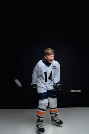 Young hockey player in white jersey number 14 kneeling on gray surface against dark background.