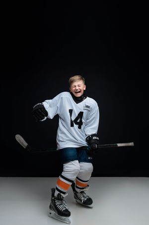 Young ice hockey player in white jersey playfully poses on black background during professional studio photoshoot.