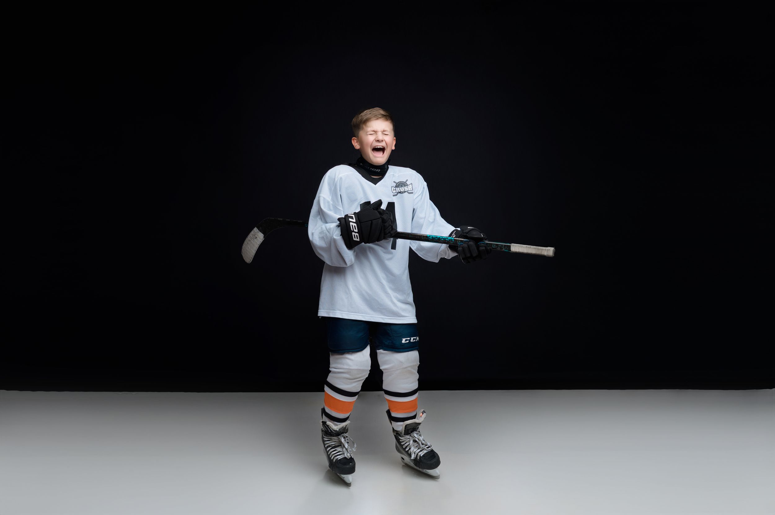 A hockey player in white uniform sits alone against a dark background demonstrating stick handling techniques.