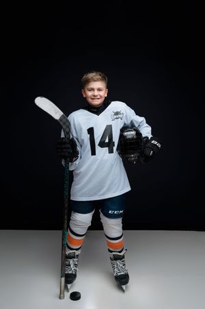 A hockey player in white jersey number 14 stands ready on the ice with a stick and puck.