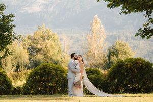 A romantic outdoor wedding photoshoot with a couple surrounded by golden sunlight and green trees in the background.