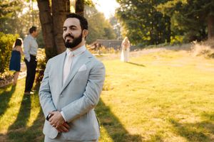 A person in a light gray suit poses outdoors in golden sunlight during sunset at a scenic outdoor location.