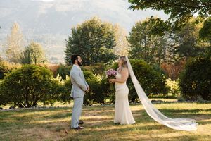 A couple walking through a sunlit garden in formal attire, with a flowing white dress trailing behind them.