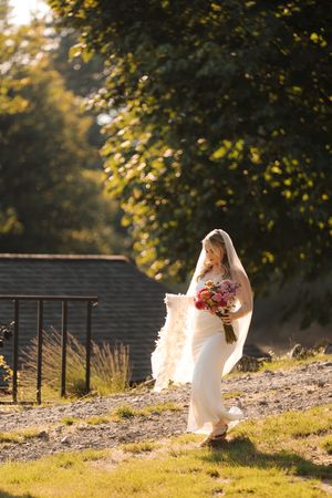 Wedding party silhouettes walk along a grassy hillside at golden hour, creating a dreamy backlit scene.