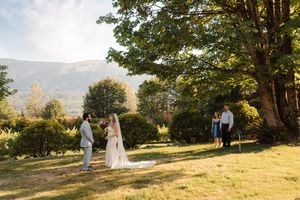 A couple walks together across a sunlit grassy hillside during golden hour with mountains in the background.