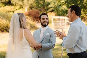 A wedding ceremony taking place outdoors in golden sunlight as an officiant conducts the service.