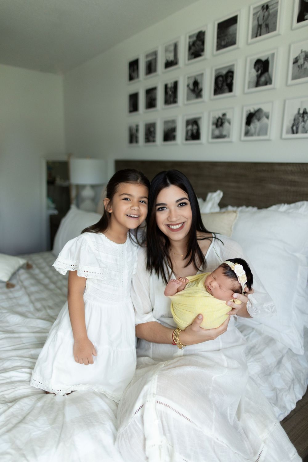 Two people sitting on a white bed sharing a joyful moment together against a wall decorated with photos.