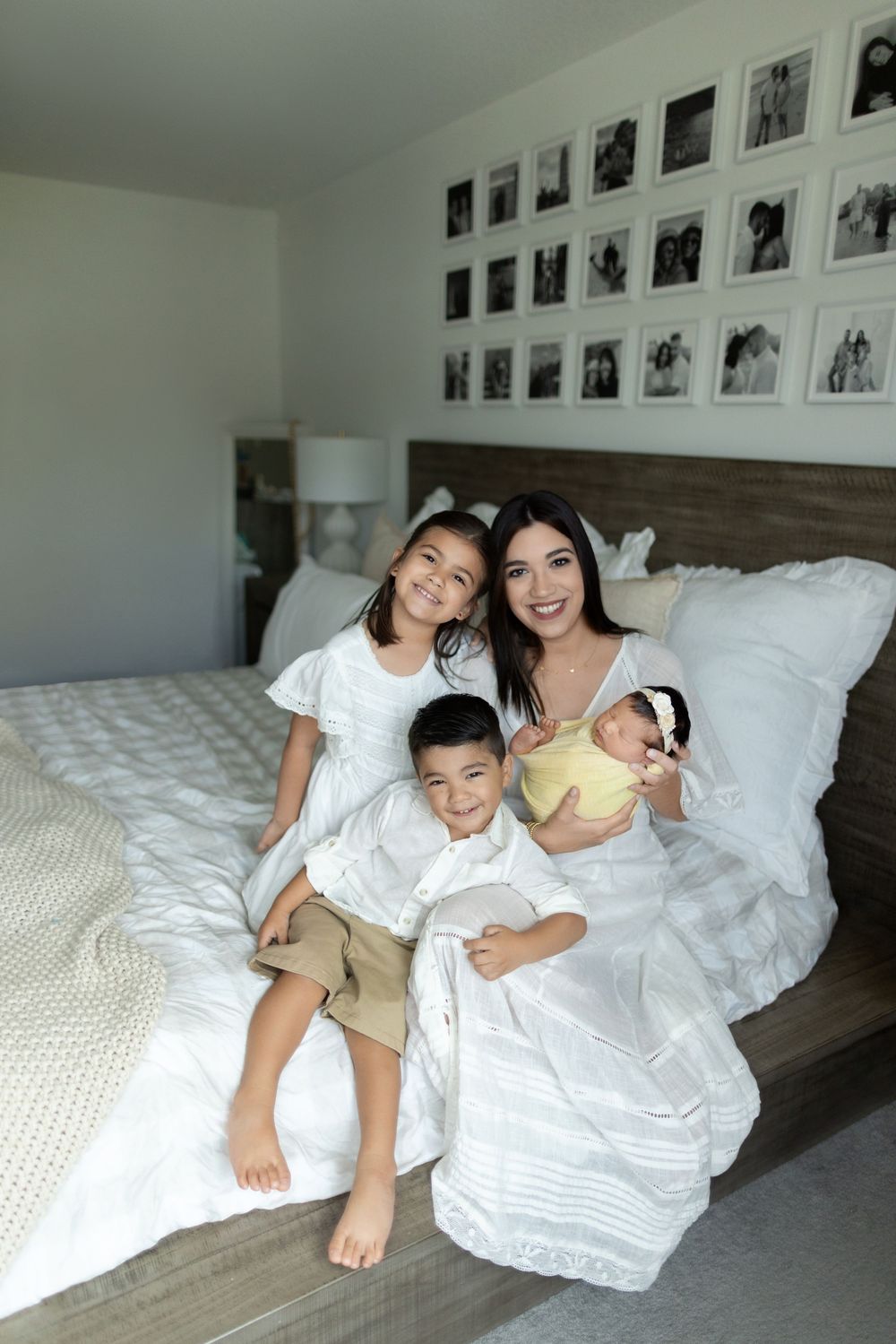 Happy people wearing white lounging on a bed surrounded by black and white photos on the wall.