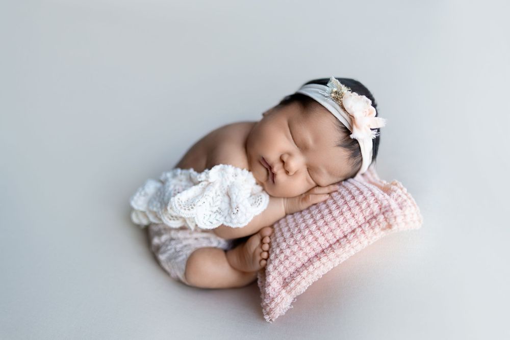 A sleeping newborn baby in white clothing rests on soft grey fabric in a series of gentle poses.
