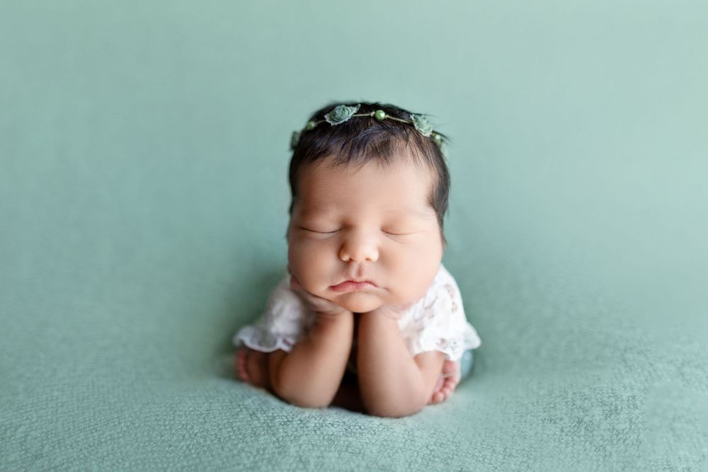A sleeping newborn wrapped in soft fabric against a mint green background in a professional studio setting.