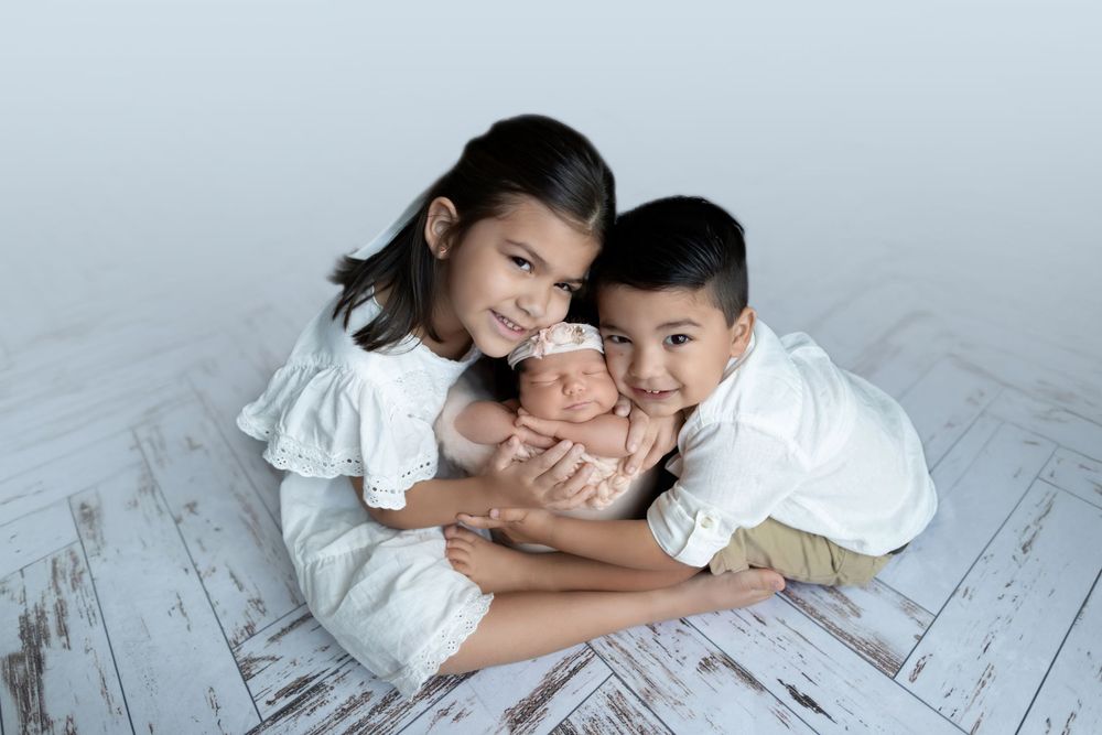 Siblings posing together on white wooden floor during a professional photo session.