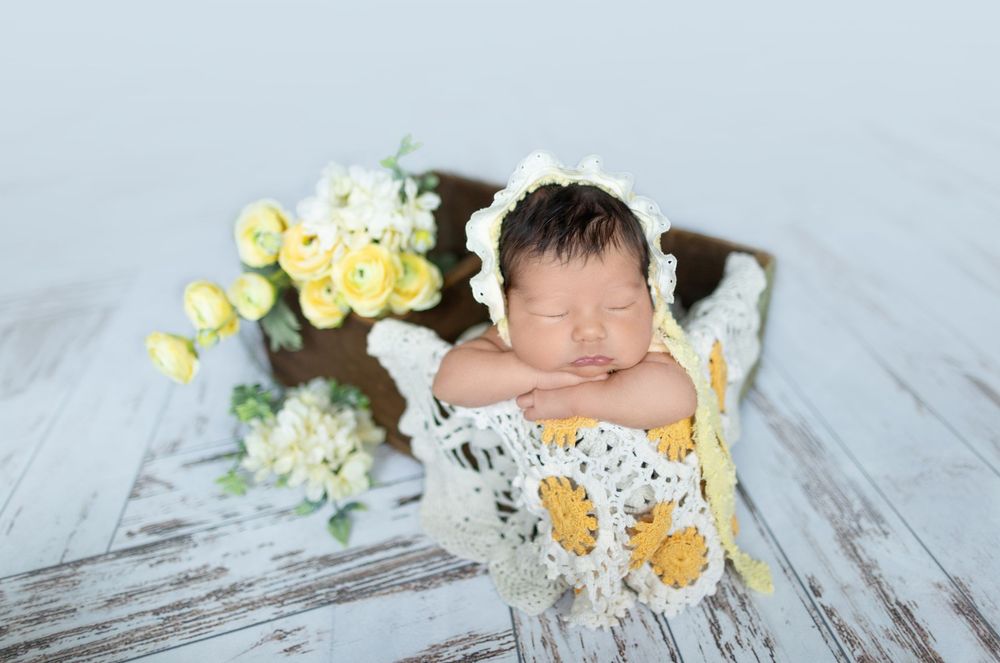 Newborn photography session featuring yellow flowers and white lace decorative elements.