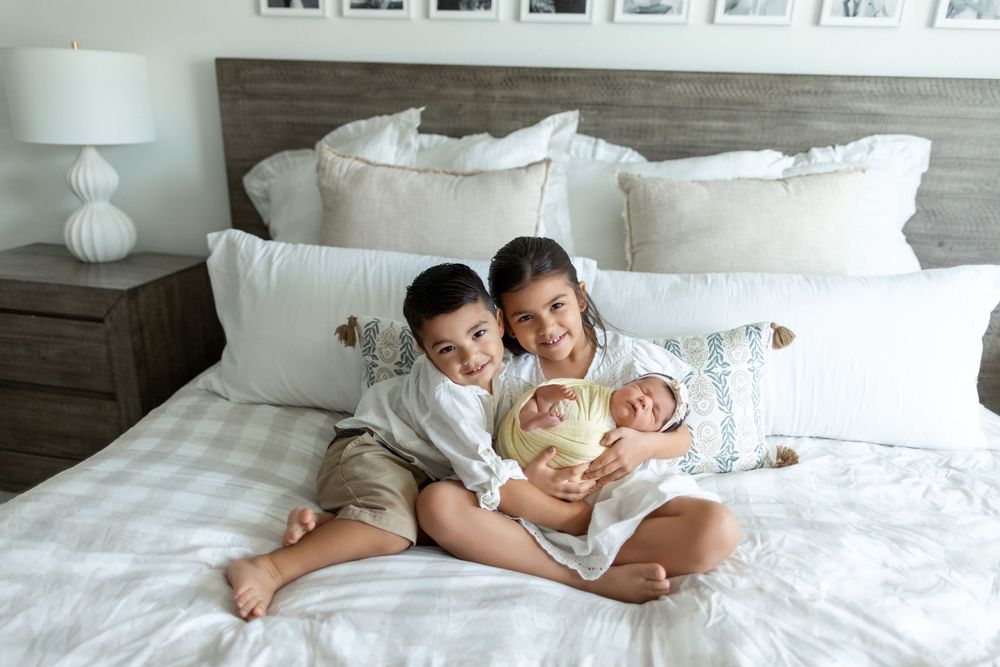 Family cuddling together on white bedding in intimate newborn photography session showing tender moments.