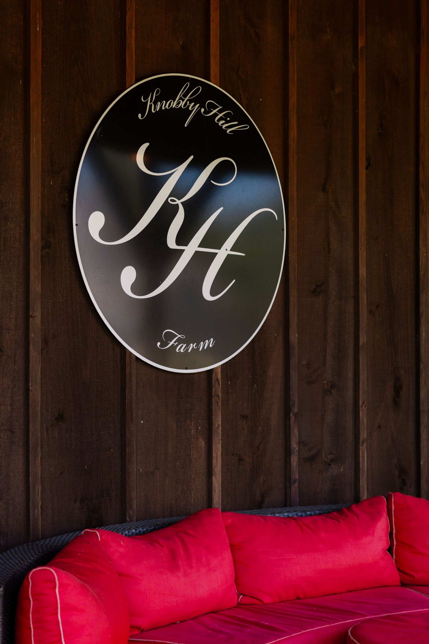 A circular wooden sign with a stylish cursive logo hangs above a bright red couch or bench against dark wood paneling.