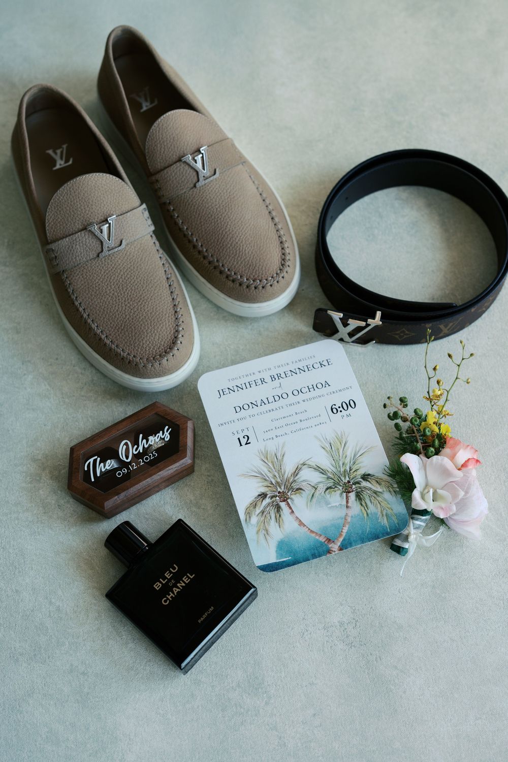 Wedding detail flatlay with brown leather shoes, invitation cards, and delicate floral accents on a light gray surface.