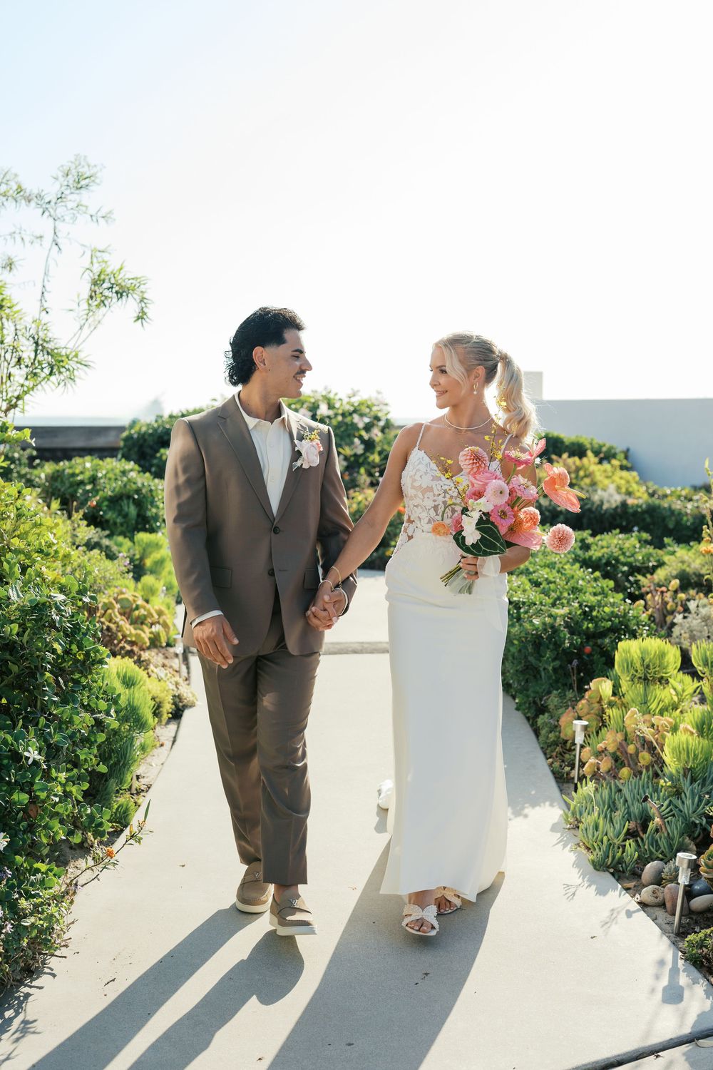 Couple taking playful poses along a white wall surrounded by lush tropical greenery.