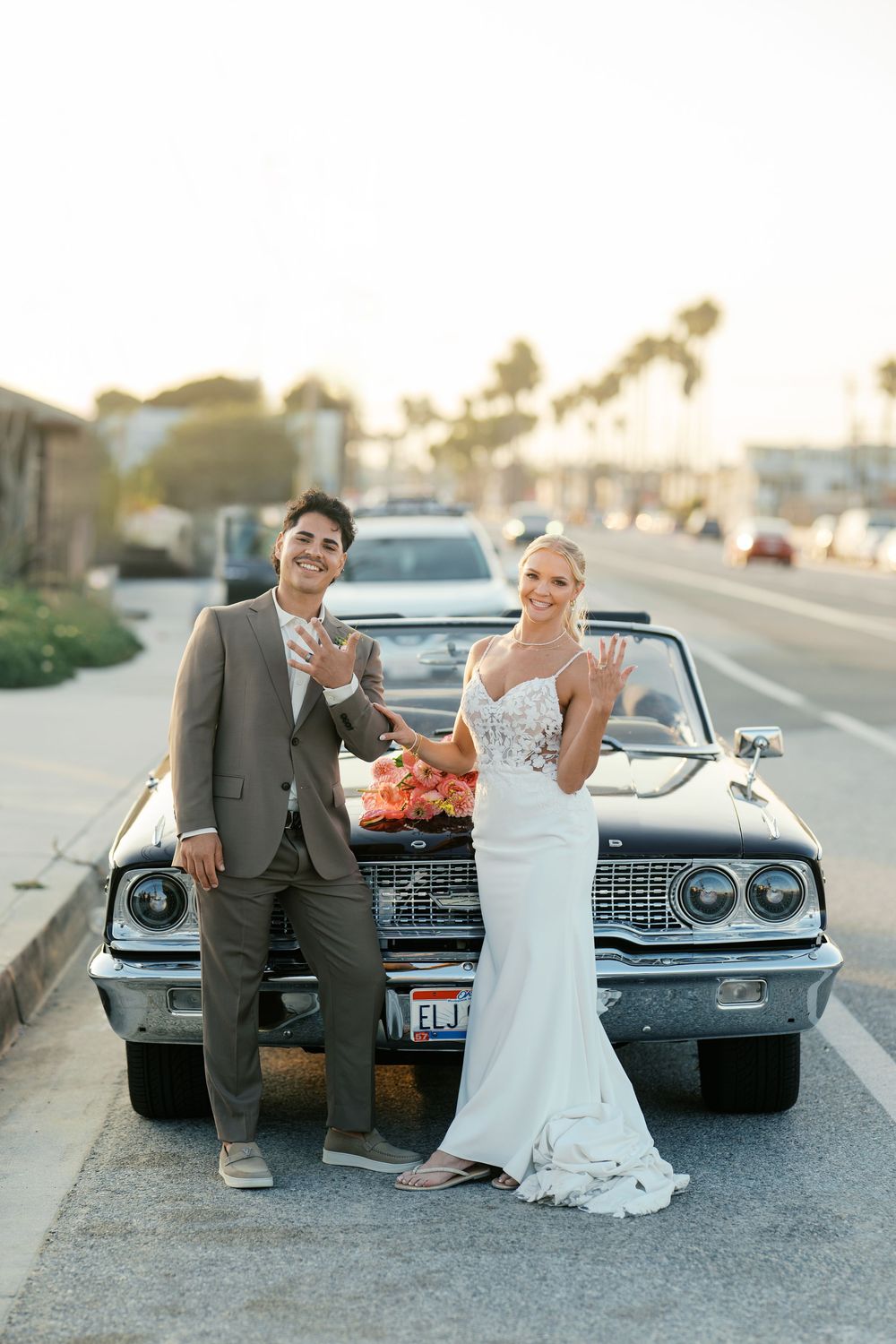 Newlyweds pose with vintage Chevrolet car during sunset photo session.
