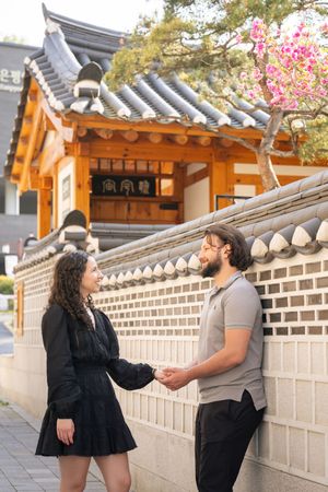 Couple sharing romantic moments along traditional Korean stone walls with cherry blossoms.