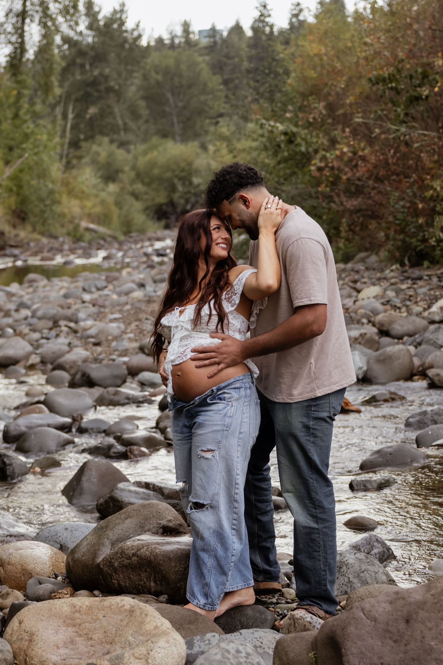 Smiling pregnant couple holding hands in field with Mount Rainier behind them taken by photographer in eatonville washington