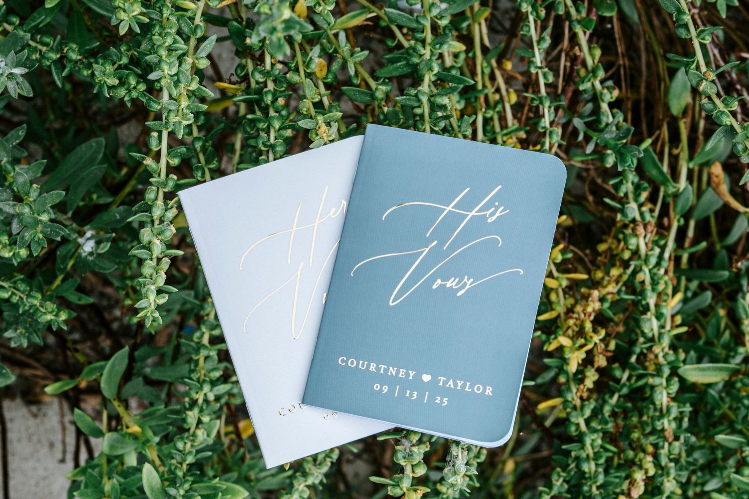 Multiple blue wedding cards arranged on green foliage background create an elegant invitation display.