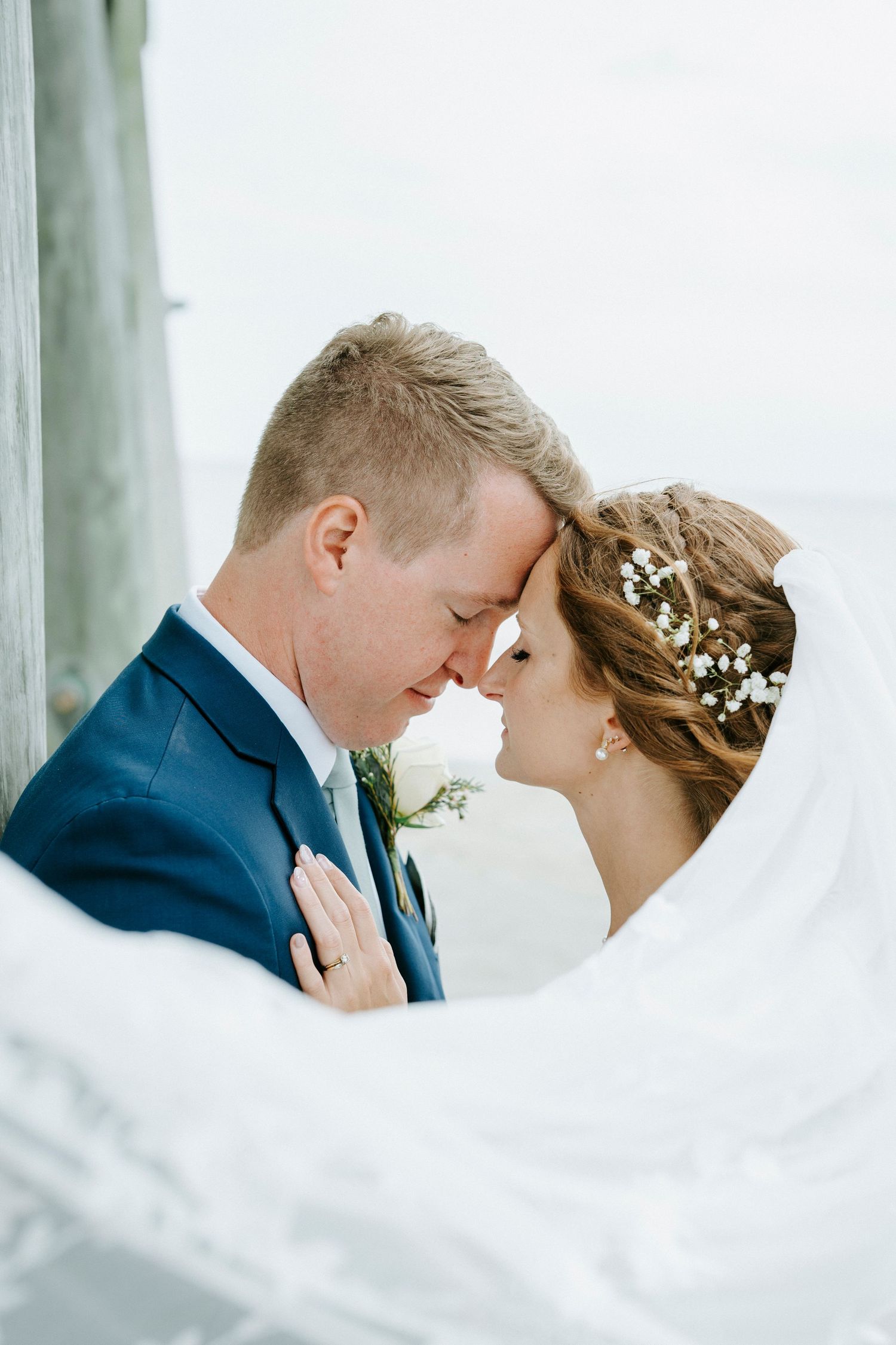 Romantic wedding portraits showing tender moments between newlyweds with flowing veil and navy suit.