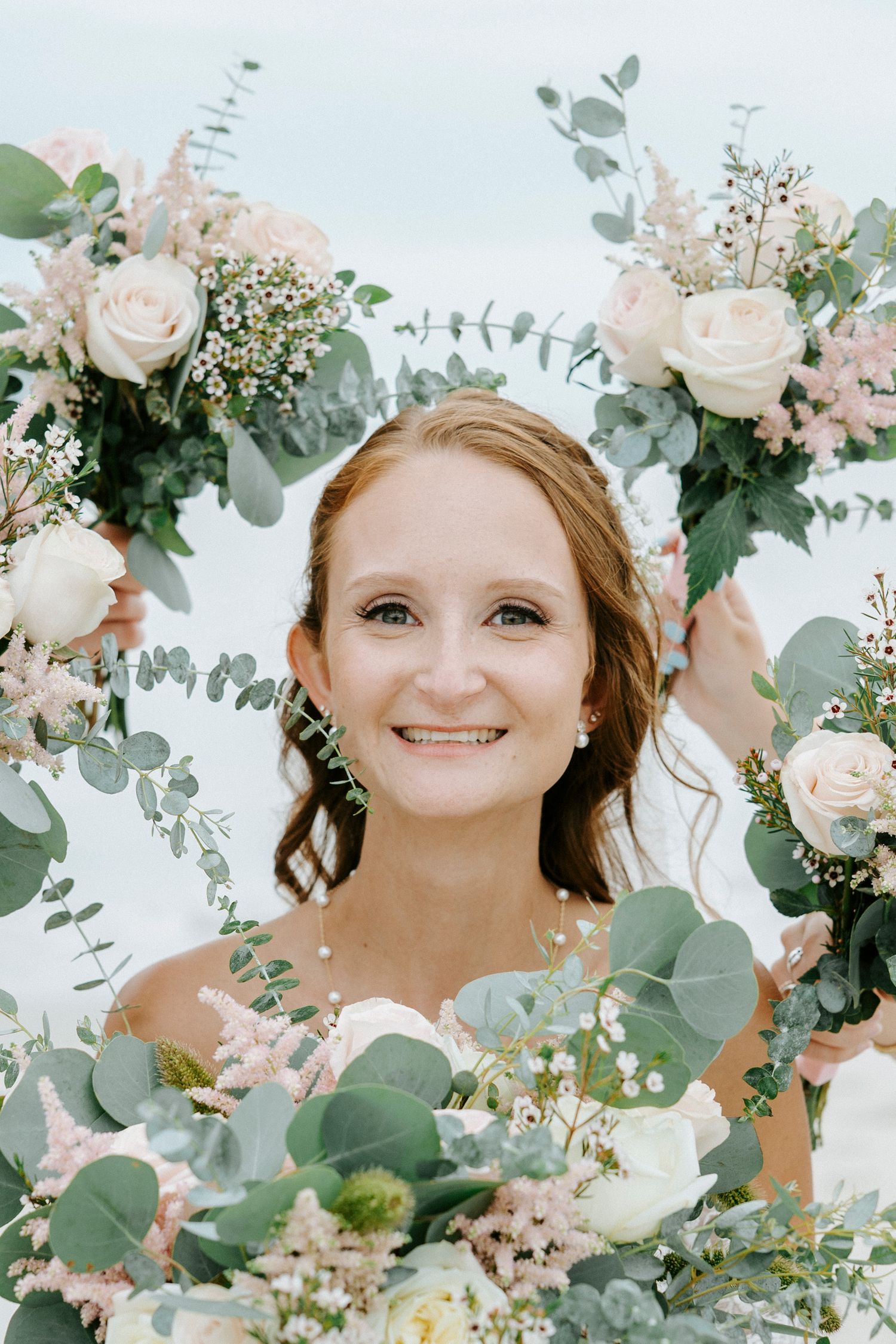 Beautiful bridal portrait surrounded by soft pink roses and eucalyptus greenery in an ethereal outdoor setting.