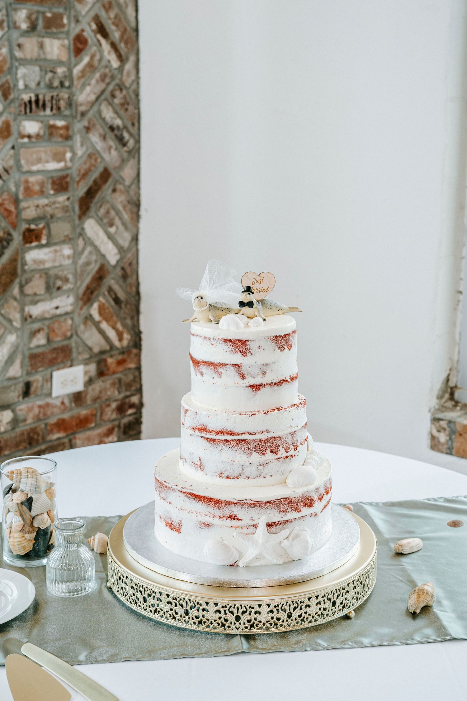 Simple semi-naked wedding cake with rose gold accents displayed on ornate white cake stand.