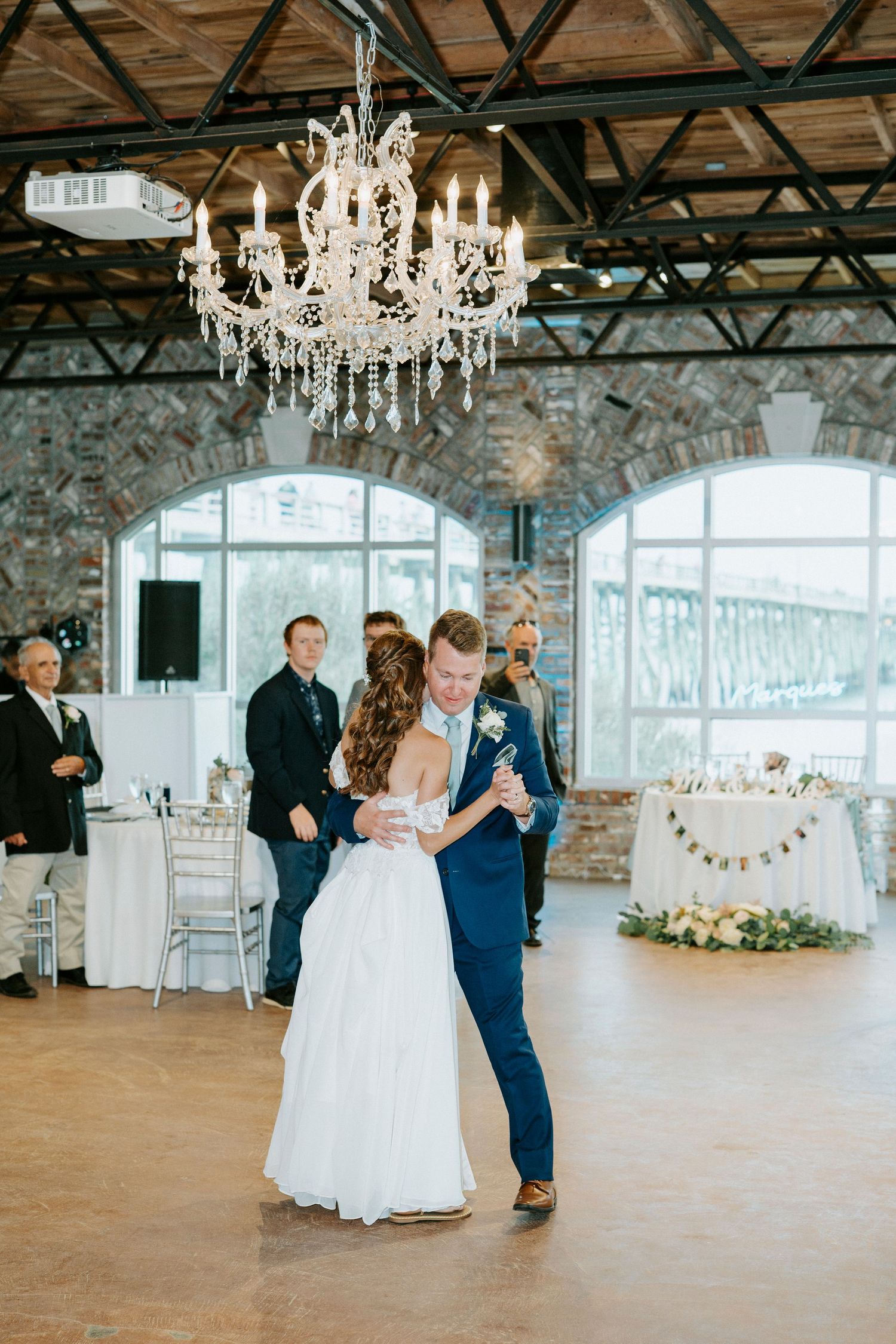 Wedding reception in an elegant industrial venue with crystal chandeliers and stone walls.