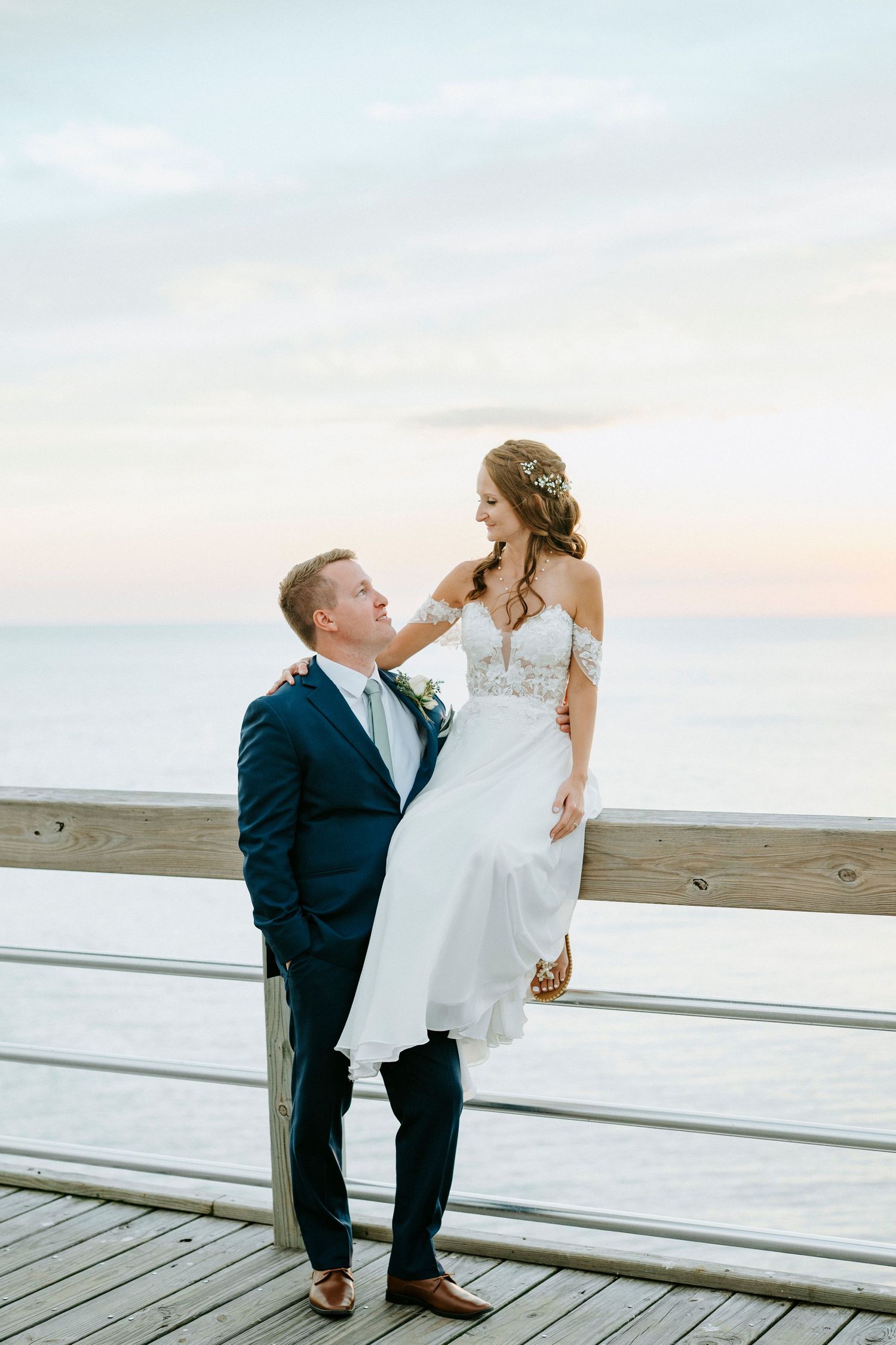A couple share a romantic moment on a wooden boardwalk at sunset with coastal views.