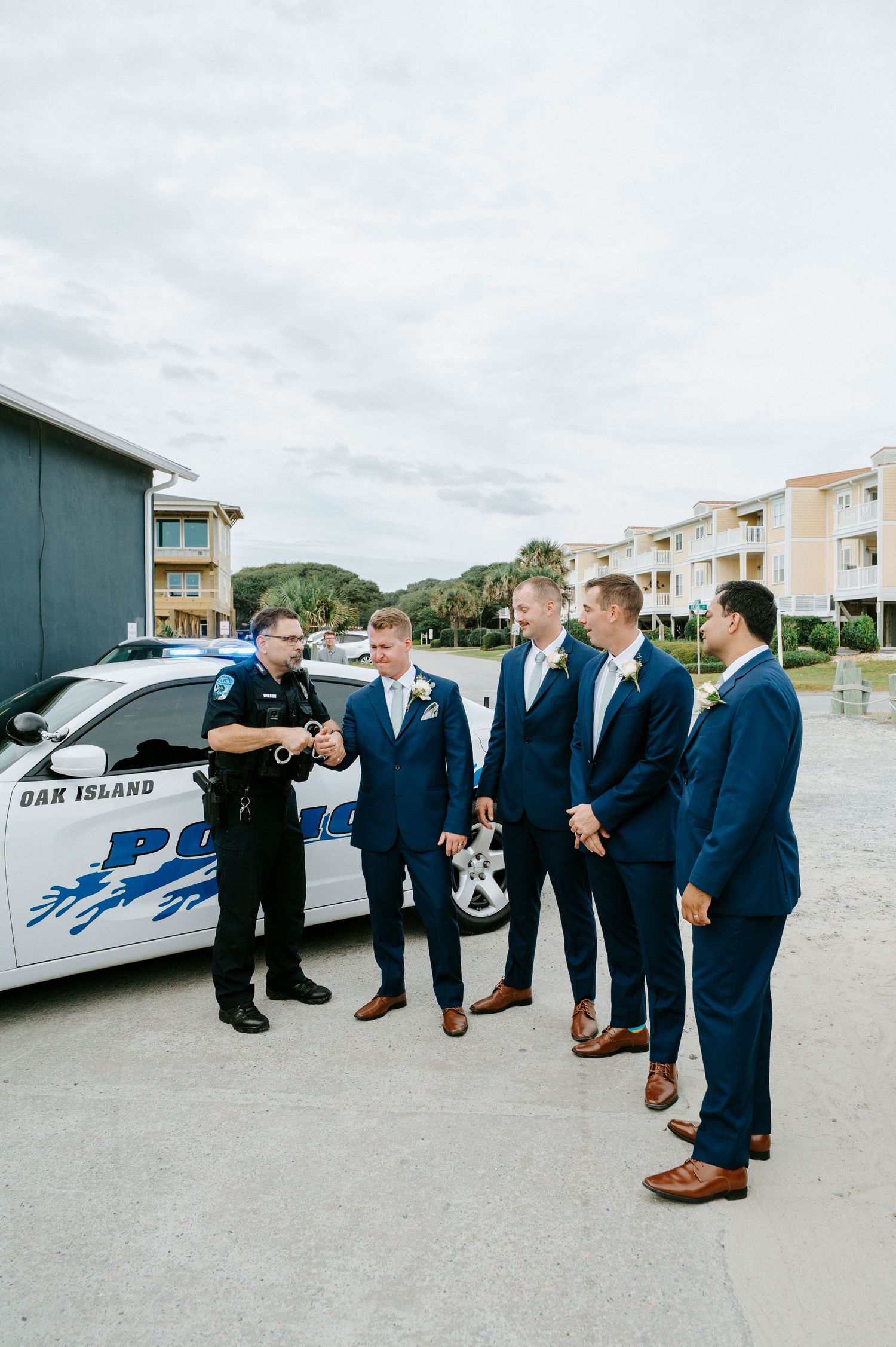 Groomsmen in navy suits line up by a police car during a wedding photoshoot.
