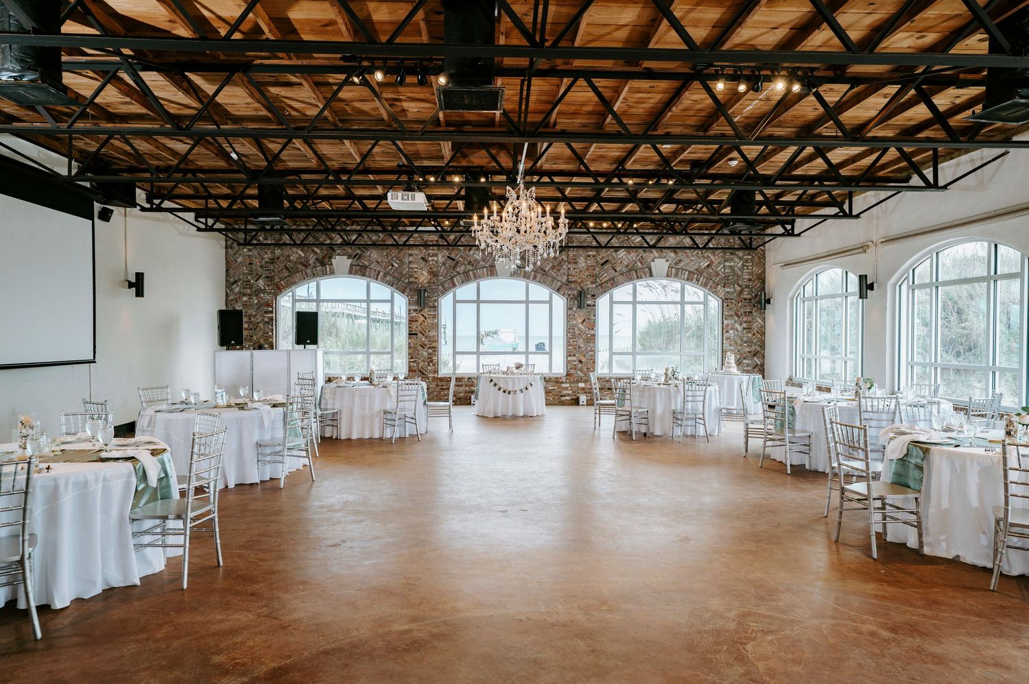 An elegant industrial wedding venue with exposed beams and chandeliers in a spacious white reception hall.