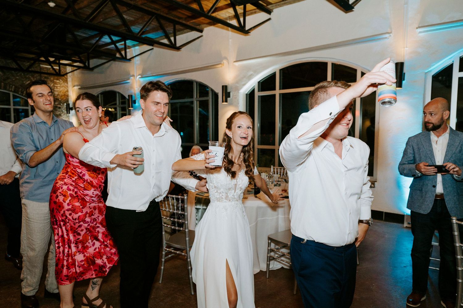 Wedding reception guests dancing and celebrating on an indoor dance floor with festive lighting.