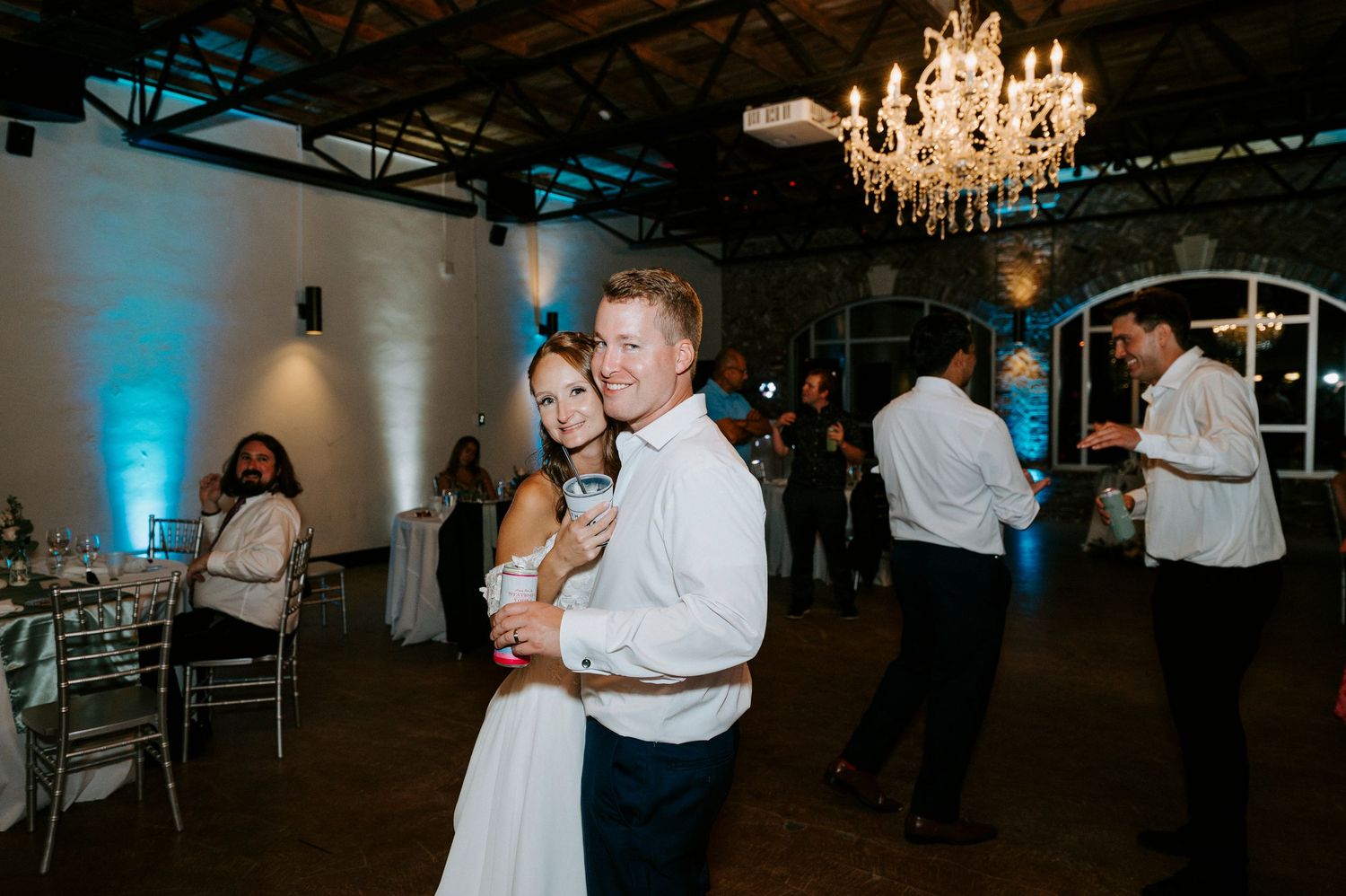 Wedding reception dance floor with chandelier lighting and guests celebrating.