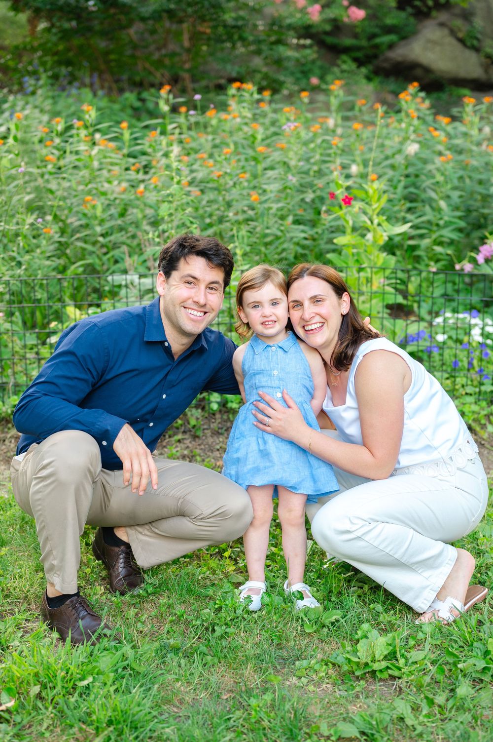 A loving family poses together on grass with yellow wildflowers blooming in a garden setting in Central Park by Westchester photographer.