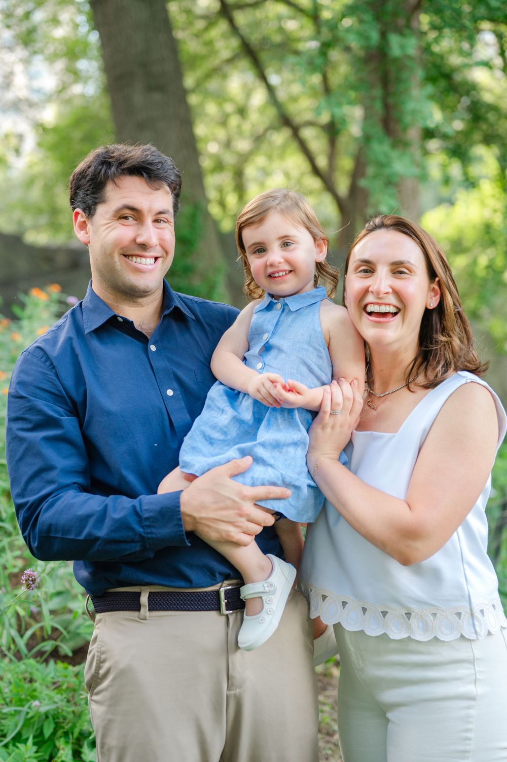 Parents holding their two-year-old daughter during a summer family photo session in Central Park.