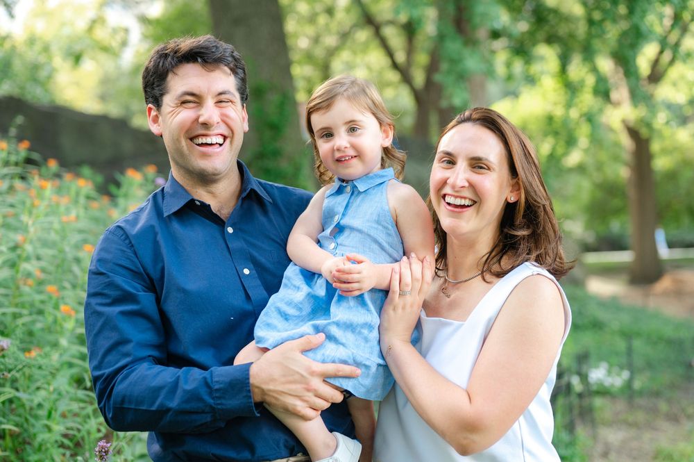 A family of three poses together outdoors in Central Park. Image by Westchester family photographer, Joliette Marie Photography.