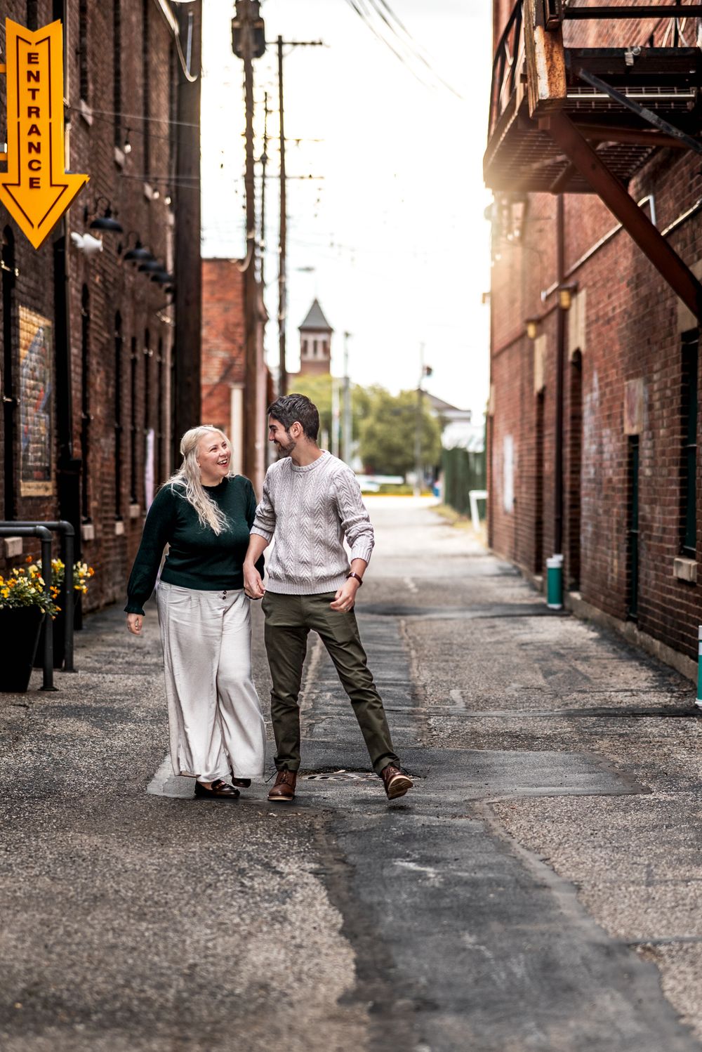 Two people walk together and chat in a charming brick alley with an orange arrow sign visible on the wall.