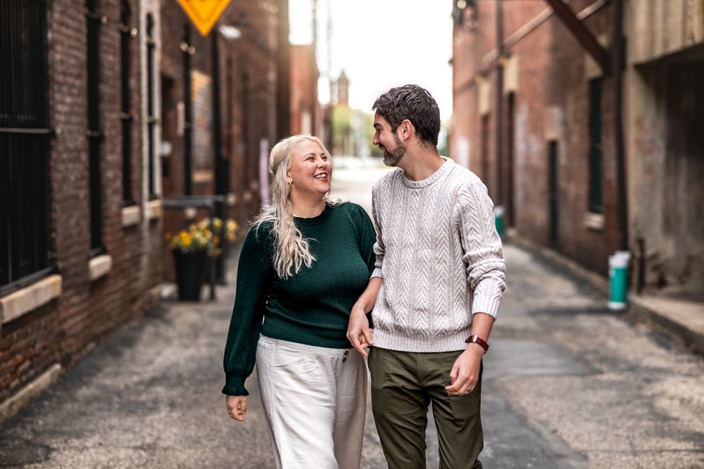 Couple walking together and laughing on a charming cobblestone street lined with historic brick buildings.