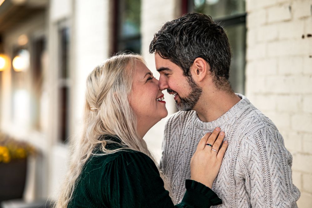 A couple shares an intimate moment while standing close together in front of a white brick wall.