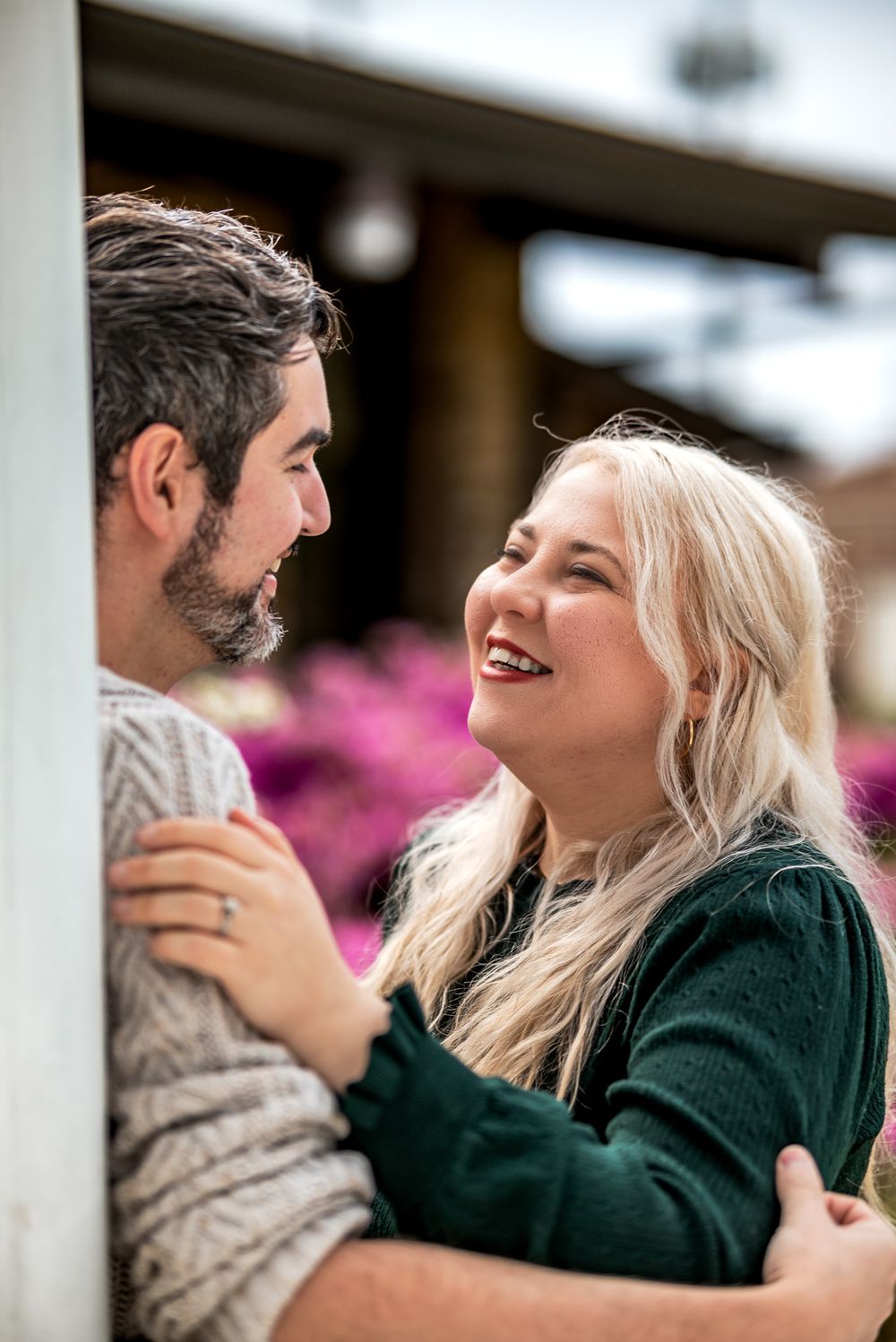 A couple laughs and embraces while wearing casual sweaters outdoors.