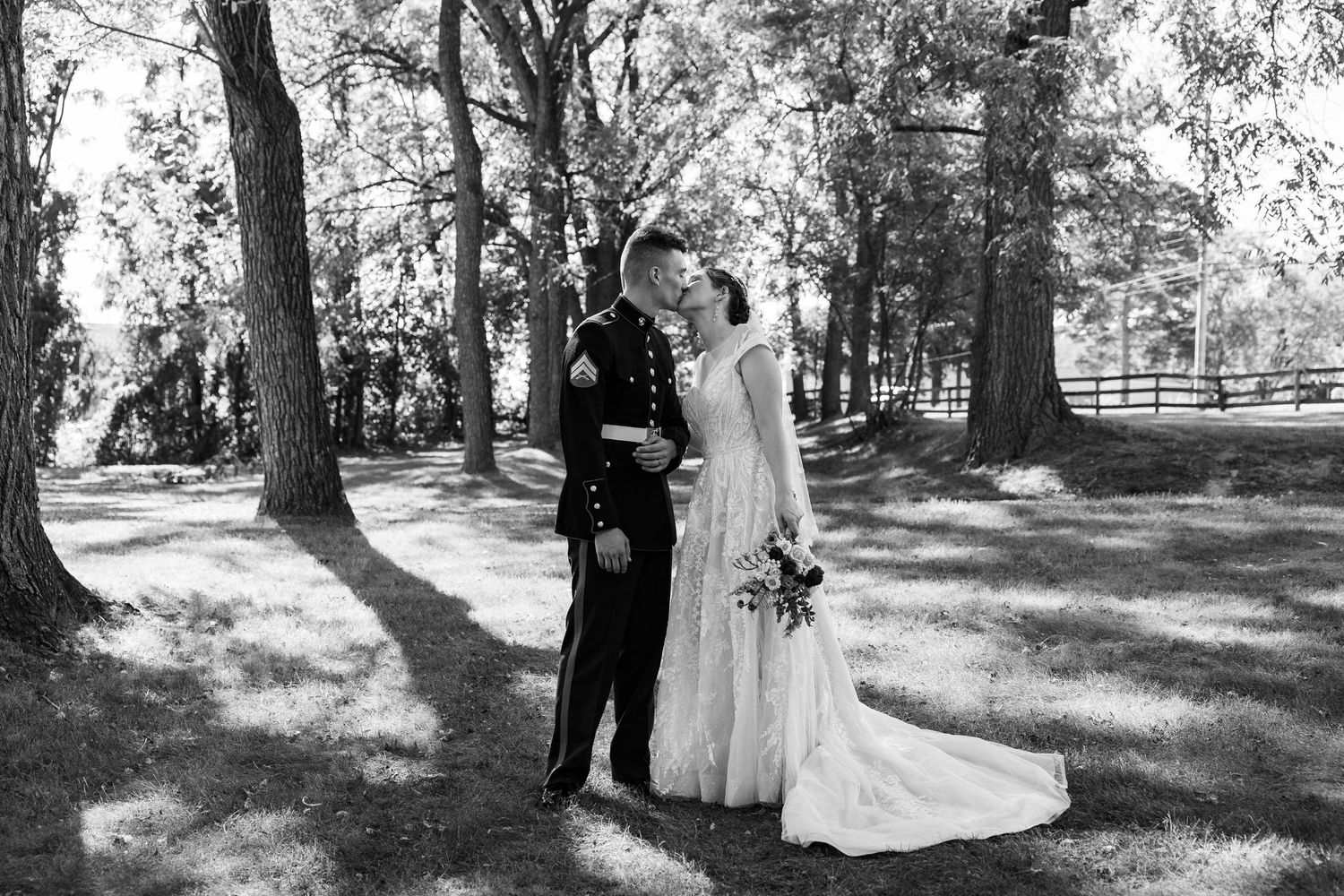 A couple shares an intimate moment together in a scenic outdoor garden setting surrounded by tall trees.
