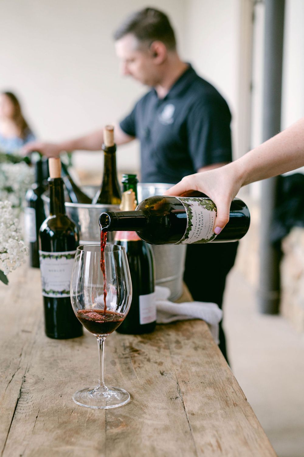 Several wine bottles and glasses are arranged on a rustic wooden table during a tasting event.