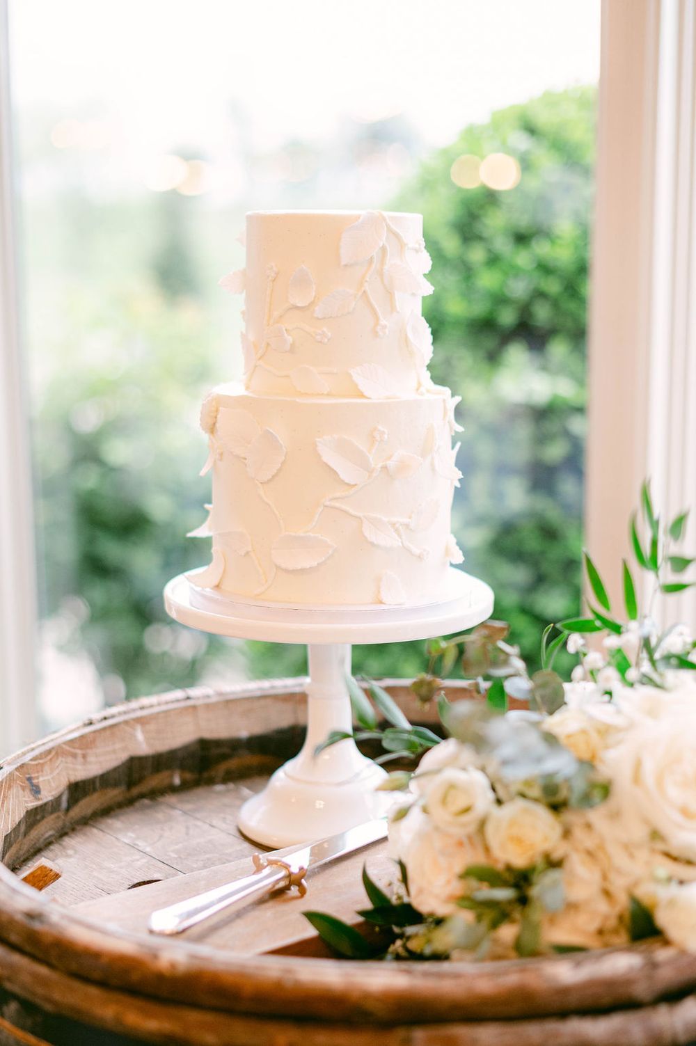 Elegant white wedding cakes displayed on rustic wooden stands with fresh roses and greenery decorations.